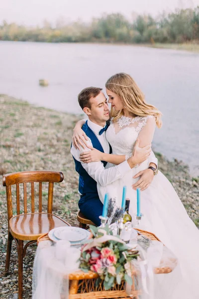 Close-up portret van de bruid zittend op de knieën van de bruidegom op de bruiloft tafel aan de kust. — Stockfoto