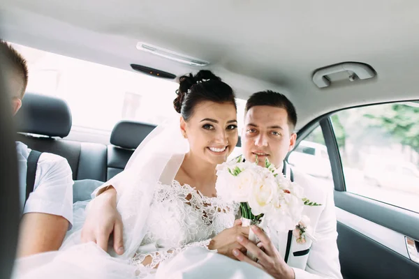 Happy newlywed couple is holding the wedding bouquet of roses while driving in the car. — Stock Photo, Image