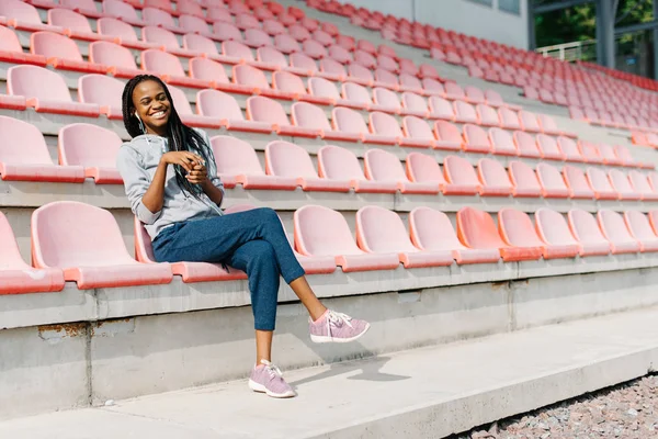 Mulher africana emocional bonita está rindo e desfrutando de música enquanto se senta nos assentos do estádio . — Fotografia de Stock