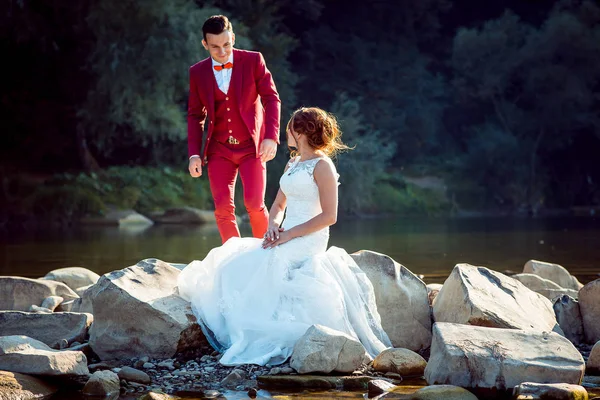 Счастливая молодожёны отдыхают у реки. Жених прекрасно говорит с невестой, сидящей на камне . — стоковое фото