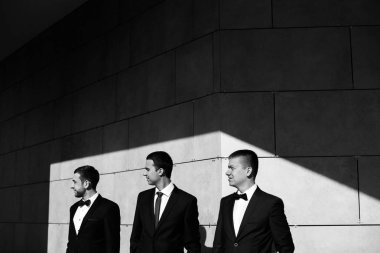 Takım elbiseli beyaz dokulu duvar poz üç emin iş adamı. Siyah ve beyaz fotoğraf