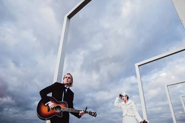 Felice sposa e lo sposo con la chitarra sullo sfondo astratto cielo blu — Foto Stock