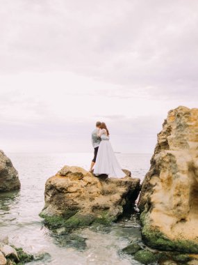 Sarılma ve deniz arasında uçurumdaki dururken gün batımını izlemek yeni evliler arkadan görünüm.