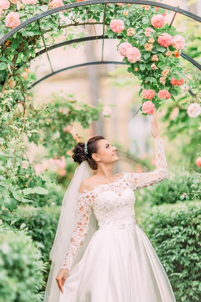 Ritratto laterale a mezza lunghezza della sposa che tocca le rose sull'arco . — Foto Stock