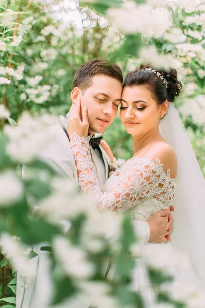 Einfühlsames Außenporträt der Frischvermählten im Garten. die Braut streicht über das Gesicht des Bräutigams. — Stockfoto