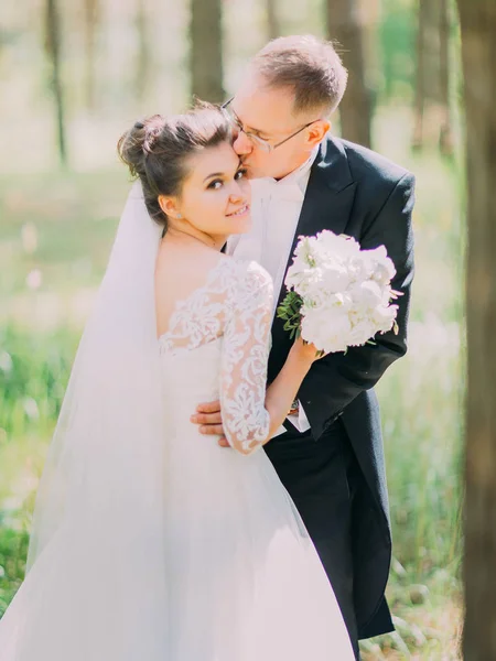 Romantiska ögonblick av brudgummen kyssa den vackra bruden i pannan. Skogsnära läge. — Stockfoto
