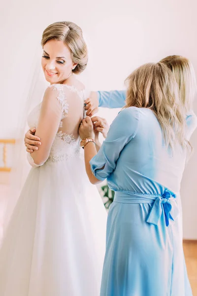 La vista lateral de las damas de honor ayudando a la novia sonriente con el vestido de novia . —  Fotos de Stock