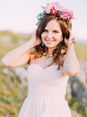 Kafasına çiçek çelenk ile gülümseyen gelin kıvırcık saçlı dokunuyor.