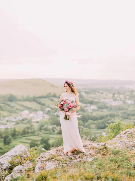 Fullängds beskåda av bruden med bröllop bukett tittar åt sidan på bakgrund av bergen. — Stockfoto