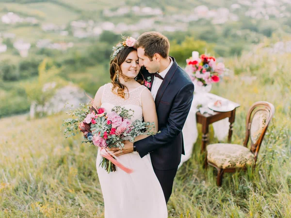 Γκρο πλαν ευαίσθητο πορτραίτο του γαμπρού αγκαλιάζει τη νύφη πίσω στα βουνά. — Φωτογραφία Αρχείου