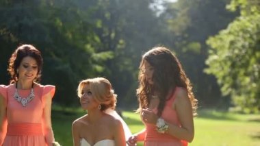 Güzel sarışın gelin onun iki çekici nedime turuncu elbiseler ile eğleniyor. Havada düğün buket atıyor. Güneşli çayır konumu.