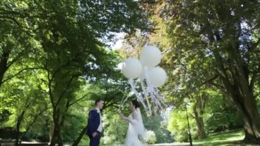 Mutlu yeni evliler şefkatle sarılma ve bahar parkta öpüşme. Gelin beyaz balon tutuyor.