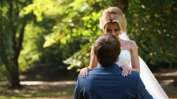 Sposi novelli ballerini nel parco soleggiato. Bello sposo sta girando in aria la sua giovane sposa bionda sorridente . — Video Stock