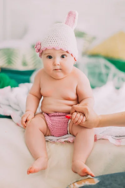 La vue verticale du bébé avec le chapeau tricoté tenant la main de la mère assis sur le lit . — Photo