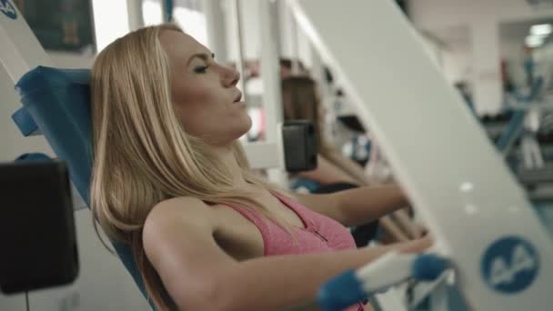 Atractiva mujer rubia atlética haciendo ejercicio en el gimnasio. Ella está haciendo ejercicios para los brazos en el entrenador. Imágenes de 4k . — Vídeos de Stock