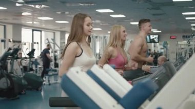 Sağlıklı ve spor kavramı içinde jimnastik salonu. Üç sağlıklı çekici sporstwoman ve sporcu tredmill üzerinde çalışan. 4k.