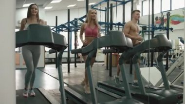 Bir kas adam ve iki sportif kadınlar eğitim koşu bandı, modern bir spor salonu vardır. 4 k görüntüleri.