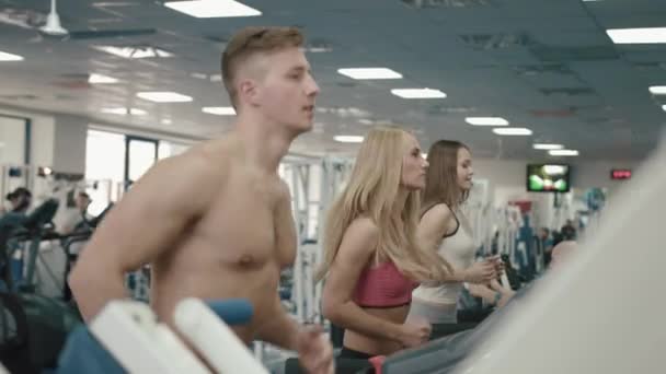 Tres mujeres atléticas y un hombre están calentando sus músculos en las cintas de correr en el gimnasio moderno. Imágenes de 4k . — Vídeos de Stock