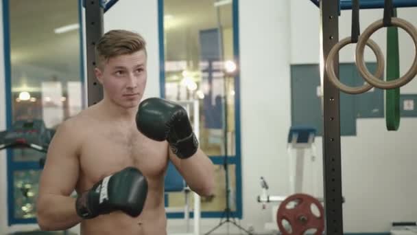 Retrato do fisiculturista muscular bonito com boxe torso nu um saco de perfuração no ginásio moderno. 4k . — Vídeo de Stock