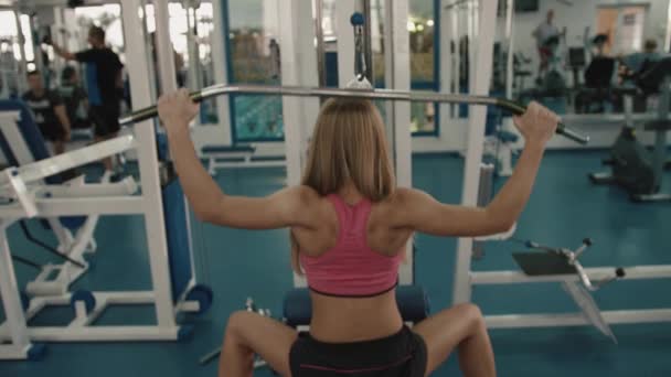 Vista trasera de la deportista rubia deportiva calentando la espalda mientras bombea hierro en el gimnasio. 4k . — Vídeo de stock