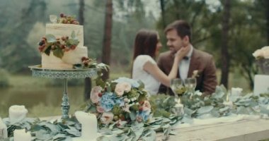 Romantik tarih kompozisyon: lezzetli pasta ve buket çiçek ile süslü masada bırakır ve mumlar vasıl şefkatle öpüşme hassas çiftin geçmiş bulanık. 4k.