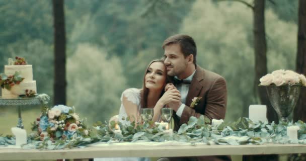 Loving para jest czule przytulanie i trzymając się za ręce podczas ich romantyczną randkę w Mglisty las. Ciasto pyszne owocowe przy stole ozdobione liśćmi, świece i kwiaty. 4k. — Wideo stockowe