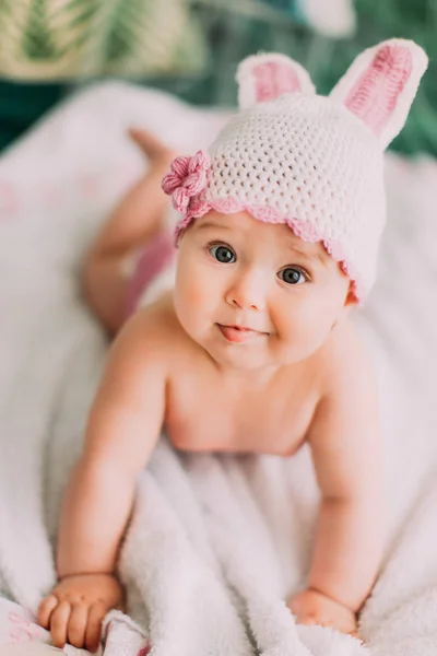 O bebezinho com olhos grandes e chapéu de malha está deitado na planície branca. Retrato de close-up . — Fotografia de Stock