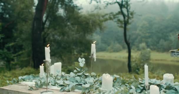 Table d'extérieur décorée de bougies foudroyantes, feuilles, fleurs et délicieux gâteau aux baies à deux niveaux. Des images 4k. Pas de gens. Forêt pouilleuse . — Video