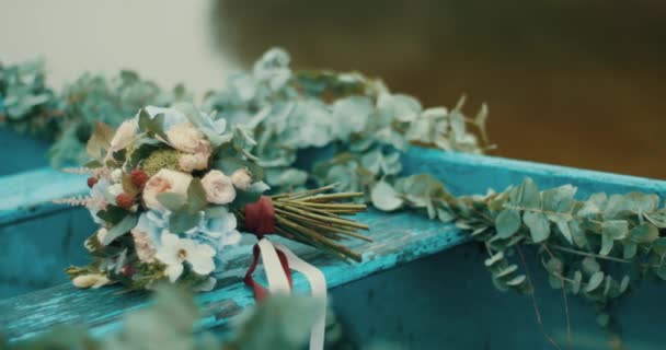 Романтическая композиция букета чудесных красочных цветов, обернутых белыми и красными ребрышками, лежащих на деревенской голубой лодке, украшенной травами. 4k . — стоковое видео