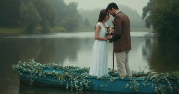 Bella coppia amorevole in stoffa d'epoca sta tenendo il meraviglioso mazzo di fiori e in piedi testa a testa mentre galleggia sul romantico decorato con erbe barca lungo il fiume nebbioso. 4k . — Video Stock