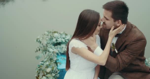 Sensible retrato de la feliz pareja adorable en el amor en tela vintage elegante flotando en el romántico barco decorado con hierbas a lo largo del lago brumoso. El hombre besa tiernamente a su amante en la cabeza . — Vídeo de stock