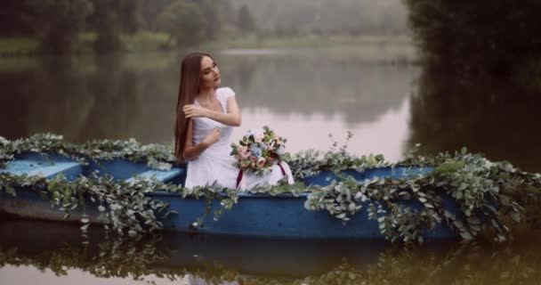 Encantadora joven en vestido blanco con hermoso ramo de flores está flotando en el barco decorado con hierbas. Río Mistry. Imágenes de 4k . — Vídeos de Stock