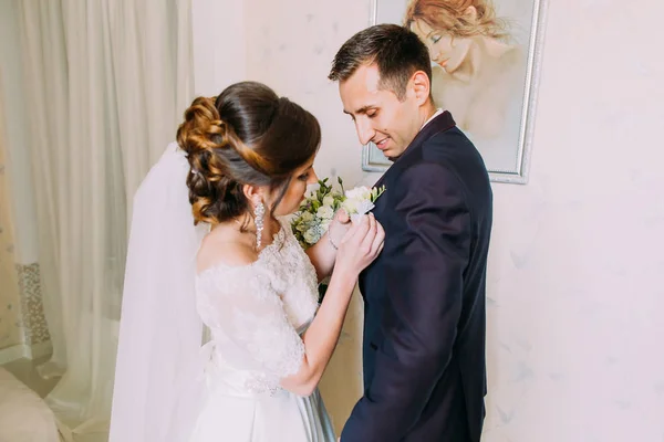 Preparazione del matrimonio. Sposa sta mettendo il boutonniere sulla giacca dello sposo sorridente . — Foto Stock