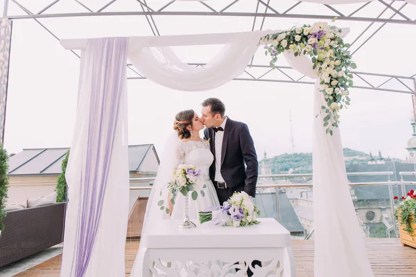 Brautpaar küsst sich unter dem Hochzeitsbogen. — Stockfoto