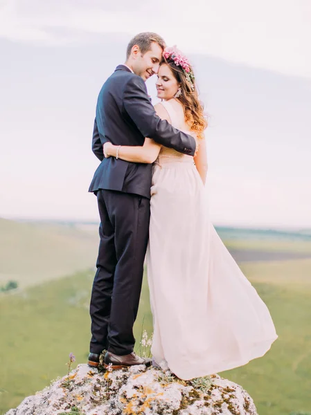 Sensible vista de los recién casados abrazados de pie sobre la piedra al fondo del prado . —  Fotos de Stock