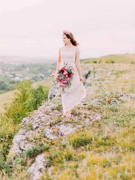 Vista a tutta lunghezza della bella sposa con l'enorme bouquet da sposa guardando da parte mentre in piedi sulle montagne . — Foto Stock