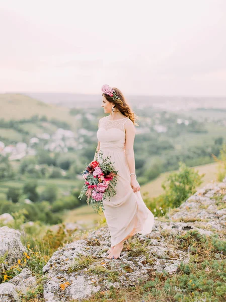 Fullängds utsikt över den vackra bruden med bröllop bukett njuter av landskapet. — Stockfoto