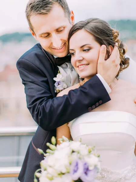 Retrato romântico de close-up. Groom está abraçando a noiva de volta enquanto acaricia sua bochecha . — Fotografia de Stock