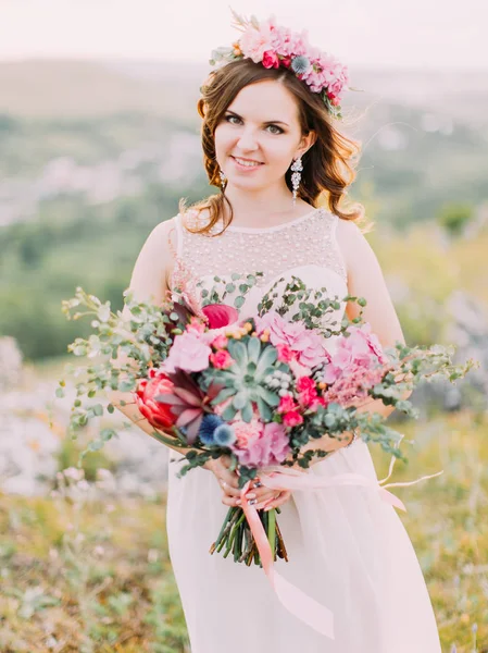 Encantadora novia alegre está sosteniendo el colorido ramo de boda enorme en las montañas . — Foto de Stock