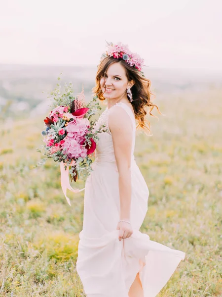 Sposa emotiva sta tenendo il bouquet da sposa e il pezzo dell'abito da sposa . — Foto Stock