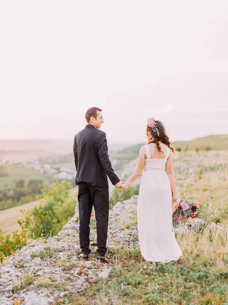 La vista trasera de la pareja recién casada abrazada caminando entre las rocas . —  Fotos de Stock