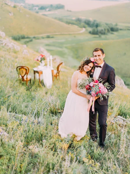 Adorável abraçar recém-casados no fundo da mesa de casamento nas montanhas . — Fotografia de Stock