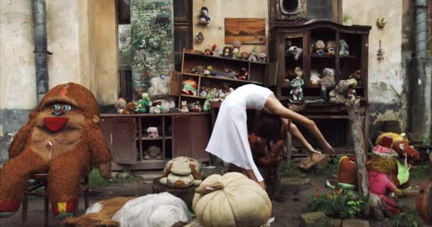 Jeune fille enfant s'étire en plein air. Elle fait des poses de ballet dans un jardin rempli de vieux jouets vintage. 4k . — Video