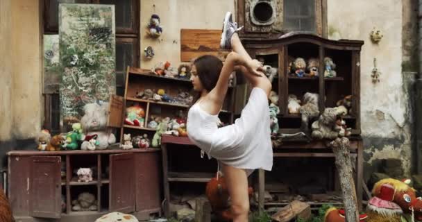 Jeune fille flexible enfant effectue des tours de ballet. Elle étire son corps dans un jardin rempli de vieux jouets vintage. 4k . — Video