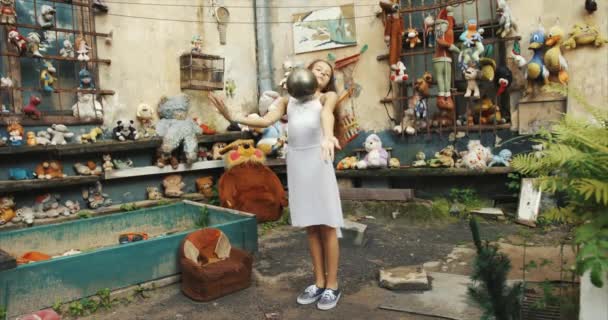 Attractive young ballerina performing dance with ball. Garden full of toys and old furniture location. 4k footage. — Stock Video