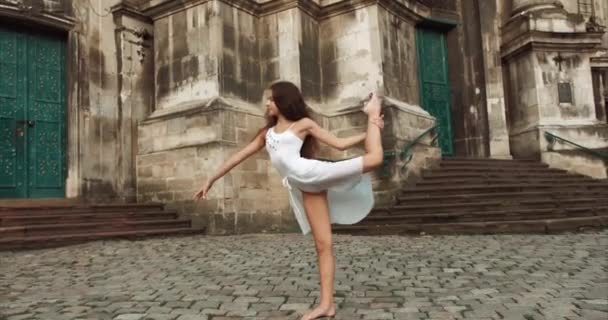 Linda menina com cabelos longos escuros é graciosamente realizando truques de balé ao ar livre. Miúdo talentoso. Filmagem 4k . — Vídeo de Stock