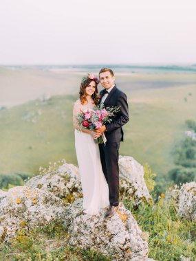 Kayaların üzerinde duran mutlu sarılma yeni evliler tam uzunlukta fotoğrafı.