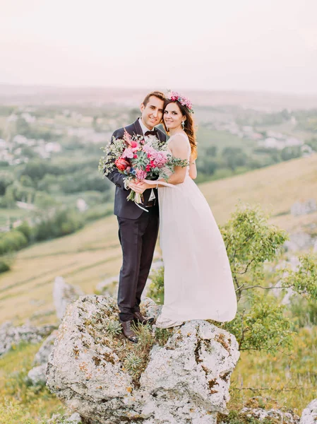 Los recién casados felices se están abrazando mientras están de pie cabeza a cabeza en las montañas. Vista de cuerpo entero . —  Fotos de Stock