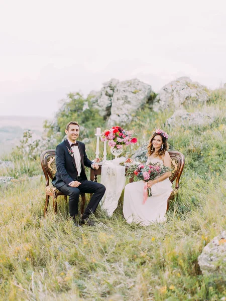 Повнометражний вид усміхненої молодої пари сидить за весільним столом у горах . — стокове фото