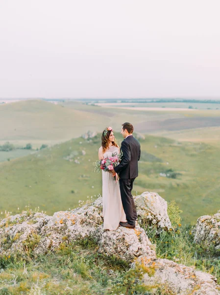 Gli sposi felici che si tengono per mano e il bouquet nuziale sullo sfondo delle verdi montagne . — Foto Stock